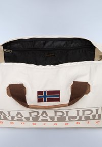 Canvas duffel taske med en cremefarvet ydre, brune håndtag og et norsk flag lap. Indvendig har den en sort lynlåslomme.