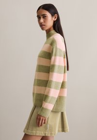 Hellgrüner und rosafarbener gestreifter Pullover mit hohem Kragen. Weiche Textur, gerippte Bündchen und Saum. Kombiniert mit einem passenden hellgrünen Rock.