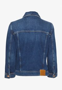 Tmavě modrá džínsová bunda s klasickým límečkem, dlouhými rukávy a knoflíkovými manžetami. Obsahuje koženou nášivku na lemu a kontrastní prošívání.