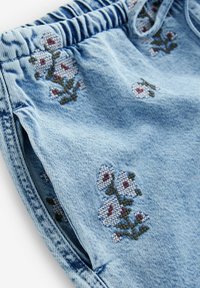 Shorts en denim bleu clair avec une taille élastique, ornés de motifs floraux brodés en blanc et bordeaux sur la surface du tissu.