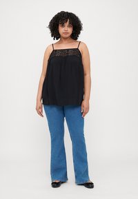 Haut sans manches noir avec des détails en dentelle au niveau du col, tissu fluide, associé à un jean évasé bleu et des ballerines noires.