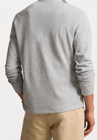 Šedý svetr s dlouhým rukávem a kulatým výstřihem, vyrobený z měkkého pleteného materiálu. Má ribbed manžety a lem, a nabízí uvolněný střih.