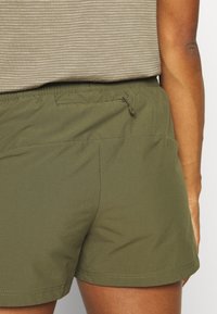 Shorts vert olive en tissu léger, dotés d'une taille élastique et d'une poche arrière zippée. Tissu lisse et design simple.