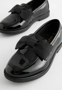 Zwarte lakleren loafers met een opvallende zwarte lintstrik over de wreef, met een ronde neus en een lage rubberen zool.