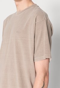Beige puuvillane T-särk, millel on ümar kaelus, lühikesed varrukad ja õrnalt tikitud LEVI'S® logo rinnal. Sile tekstuur ja mugav lõige.