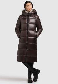 Long puffer coat in dark brown with a hood, horizontal quilted design, zip closure, side pockets, and durable fabric.