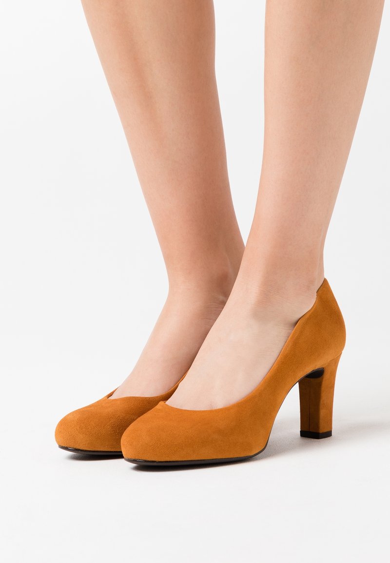 Escarpins en suède à talons hauts orange, avec un bout rond, un design découpé sur les côtés et un talon carré pour la stabilité.