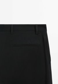 Black trousers featuring a flat waistband, belt loops, and a single back pocket with a subtle stitched border, made from smooth fabric.