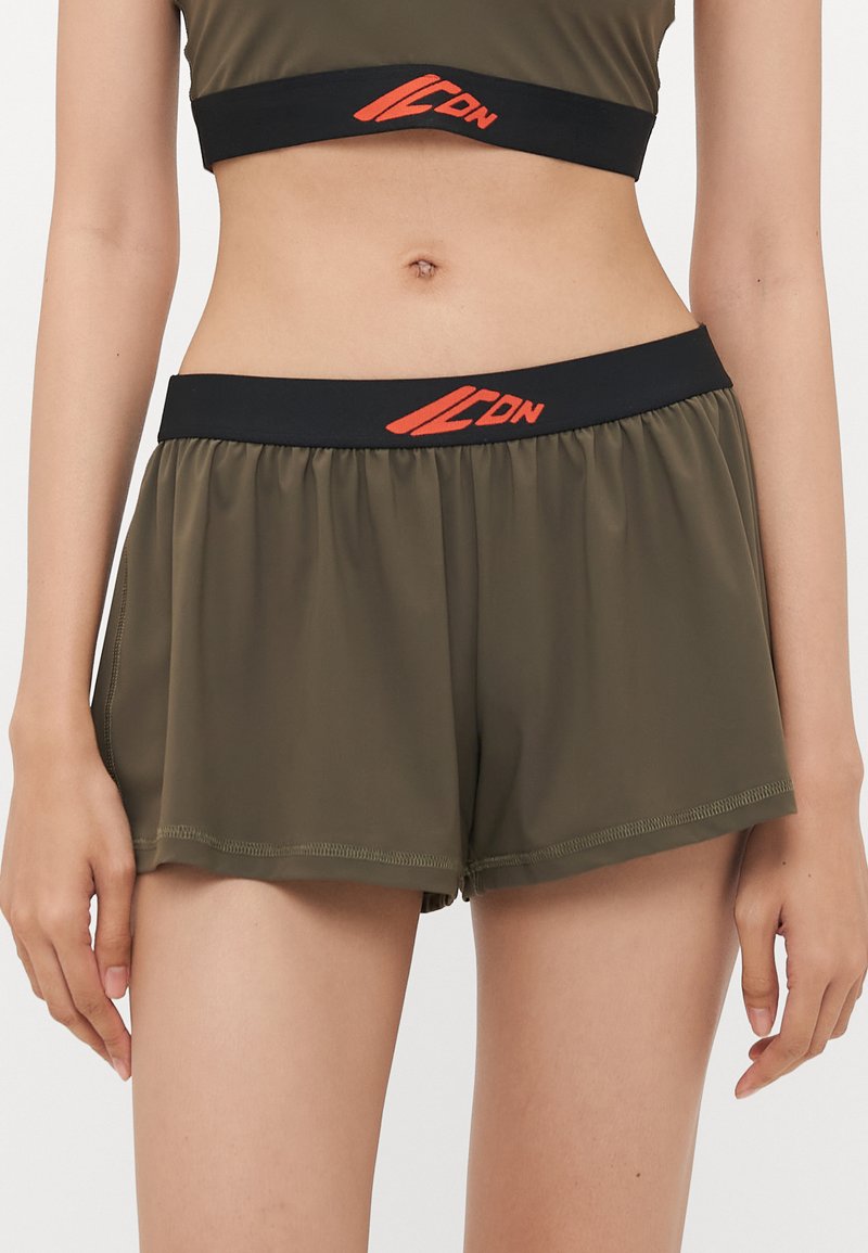 Olive green sports shorts with a black waistband featuring an orange logo. The fabric is lightweight and smooth, with a relaxed fit.