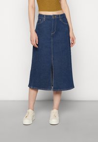 Tummansininen denim-midi-hame, jossa on etureikä, viisi taskua ja kontrastivärinen ompelu, yhdistettynä valkoisiin tennareihin.