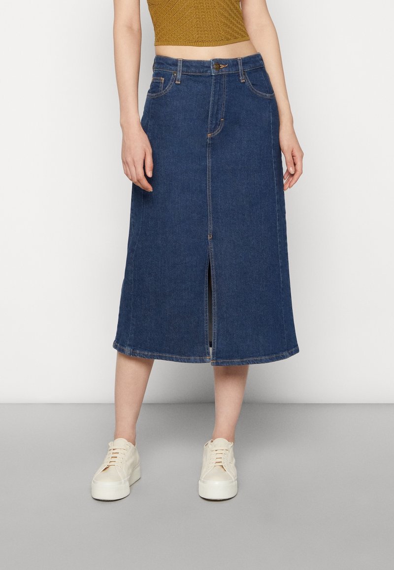 Tummansininen denim-midi-hame, jossa on etureikä, viisi taskua ja kontrastivärinen ompelu, yhdistettynä valkoisiin tennareihin.