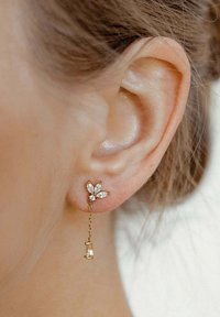 Goldfarbene Tropfohrringe mit floralen Motiven, klaren Strasssteinen, einer Kettenverbindung und einem kleinen Akzentstück am unteren Ende.