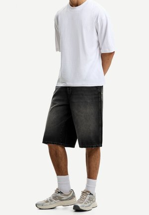 Personne portant un t-shirt blanc uni oversize, un short en jean noir mi-cuisse, des chaussettes blanches montantes et des chaussures de course beiges.