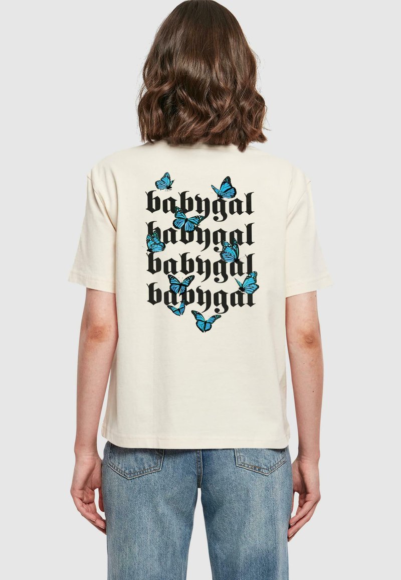 Kremfarget t-skjorte med grafisk design som har gjentatt "babygal" tekst og spredte blå sommerfugler på baksiden. Korte ermer.