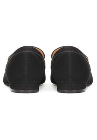 Paire de mocassins en daim noir vus de dos, avec des talons bas et des coutures visibles le long de la couture centrale.