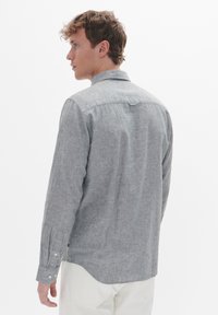 Grijze button-up shirt met lange mouwen, subtiele textuur en achterkant yoke detail. Voorzien van witte knopen en een gebogen zoom.