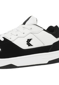 Black and white athletic shoes with a leather and suede upper, padded collar, laces, and a prominent logo on the side. Flat rubber sole.