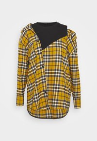 Chemise asymétrique à manches longues à carreaux jaune et noir avec un empiècement noir aux épaules et une partie avant partiellement déboutonnée.