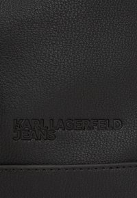 Black textured leather featuring embossed "KARL LAGERFELD JEANS" branding. Smooth finish with a subtle sheen. Minimal stitching detail.
