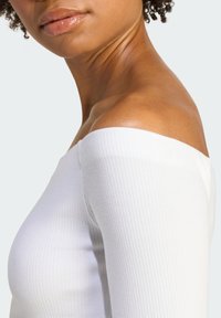 Biele rebrované top bez ramienok s priliehavým strihom, ktorý vystihuje hladkú textúru a čistý, minimalistický štýl.