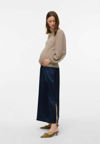 Abbigliamento per maternità con una maglia beige textured con maniche a sbuffo, una gonna in satin blu navy con spacco e scarpe verde oliva a punta.