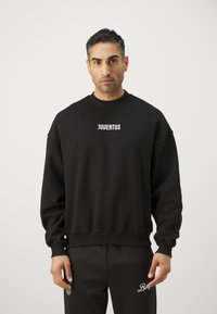 Sudadera negra con cuello redondo y hombros caídos, con la palabra "JUVENTUS" en texto blanco en la parte delantera. Tejido suave y texturizado.