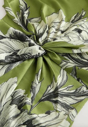 Zelená látka se strukturovaným povrchem s černobílými květinovými motivy, uspořádanými do krouceného vzoru.
