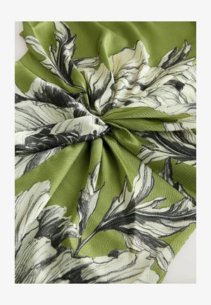 Grønt stof med en struktureret overflade, der har sorte og hvide blomsterprint arrangeret i et snoet mønster.