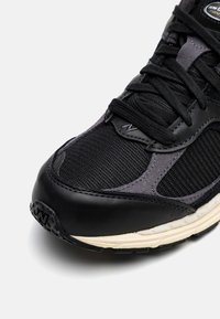 Baskets noires et gris foncé en mesh et cuir, avec un bout rond, une surface texturée et des accents subtils ; conçues pour le confort et la stabilité.