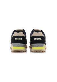 Marineblaue und beige Sneakers mit einem strukturierten Stoffoberteil, das eine graue Zwischensohle und einen leuchtend gelben Akzent nahe der Außensohle aufweist. Markenlogo sichtbar.