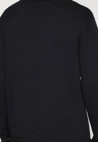 Black knitted sweater with a textured pattern, featuring a round neckline and loose fit. The back has a seamless design and is unadorned.
