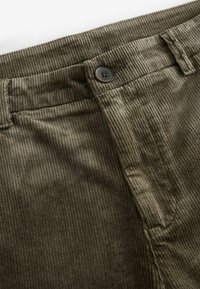 Pantalon en velours côtelé vert olive foncé avec une ceinture visible, des passants de ceinture, une fermeture par un bouton unique et des détails de couture sur la poche avant.
