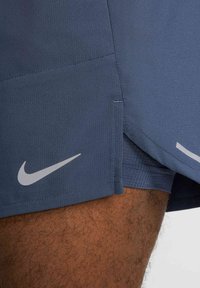 Pantalones cortos Nike de color azul oscuro con una tela texturada, aberturas laterales y un logotipo blanco prominente en la parte inferior izquierda.