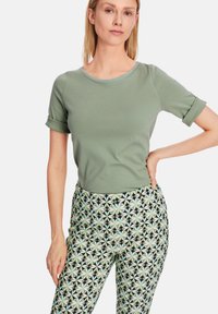 Grünes kurzärmliges Oberteil mit rundem Halsausschnitt, kombiniert mit gemusterten Hosen, die geometrische Formen in Grün und Schwarz aufweisen.