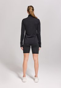 Zwarte lange mouwen top met een hoge hals en een fitted ontwerp, gecombineerd met zwarte shorts, die een soepele textuur en een sportieve stijl tonen.