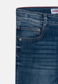 Jeans i mörkblå denim med en slät yta. Funktioner inkluderar fem fickor, bronsfärgad hårdvara och synliga sömnadsdetaljer.