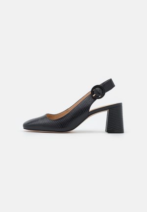 Zapato tipo pump negro texturizado con tira trasera de hebilla redondeada y tacón ancho, mostrado de lado sobre un fondo neutro.