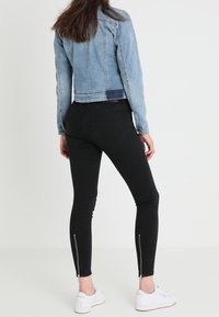 Džínová bunda v světle modré barvě, kratší střih s dlouhými rukávy. Černé skinny džíny se zipy na kotnících a bílé tenisky.