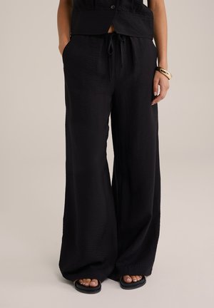 Zwarte wijde broek van textiele stof met een elastische tailleband, voorzien van zijzakken en een ontspannen pasvorm.