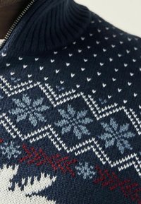 Pull en maille navy avec un col haut, présentant des motifs géométriques en rouge, blanc et bleu clair, incluant des flocons de neige et des cœurs.