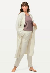 Cardigan lungo color crema, pantaloni tapered abbinati e una maglietta a maniche corte color malva. Tessuto morbido, vestibilità rilassata, con tasche laterali sul cardigan.