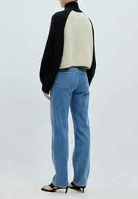 Gehaakte trui met een hoge kraag, met een zwarte voorkant en een crèmekleurige achterkant. Gecombineerd met lichtblauwe rechtliggende jeans en zwarte hak sandaaltjes.