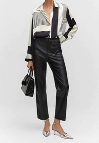 Czarna i biała bluzka w paski z długimi rękawami, zestawiona z czarnymi spodniami z ekoskóry o wysokim stanie oraz srebrnymi szpilkami. Czarna torebka.