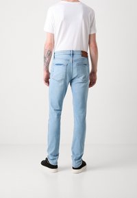 Vaqueros de mezclilla azul claro con un corte ajustado, cinco bolsillos y un parche de cuero en la parte trasera de la cintura. Textura suave y longitud estándar.