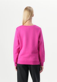 Fuchsia sweatshirt med rund hals, lange ermer og ribbede mansjetter. Laget av mykt materiale, har den en avslappet passform og et rent design.