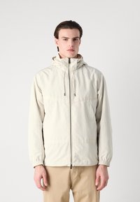 Jachetă impermeabilă ușoară de culoare bej, cu fermoar frontal, glugă ajustabilă, mansete elastice și design minimalist. Potrivită pentru îmbrăcăminte casual.