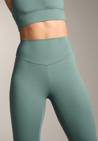 Leggings atletice de culoare verde deschis, realizate dintr-un material elastic, având talie înaltă, textură netedă și cusături plate pentru confort.