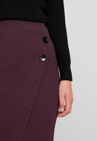 Burgundská sukně s bílými puntíky, která má boční knoflíkovou klopu v černé barvě. Hladký materiál s přiléhavým střihem.