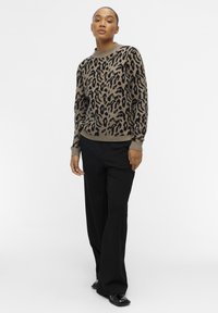 Pull en imprimé léopard marron et noir, en tissu tricoté, encolure ras du cou, poignets côtelés, associé à un pantalon large noir et des chaussures brillantes.