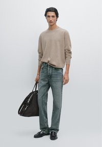 Brązowy sweter dzianinowy, wyblakłe niebieskie dżinsy, czarne buty i ciemnobrązowa torba na ramię. Gładkie tekstury i luźny fason.